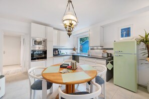 A modern kitchen with white cabinets, a green refrigerator, a wooden dining table with chairs, and a hanging light fixture.