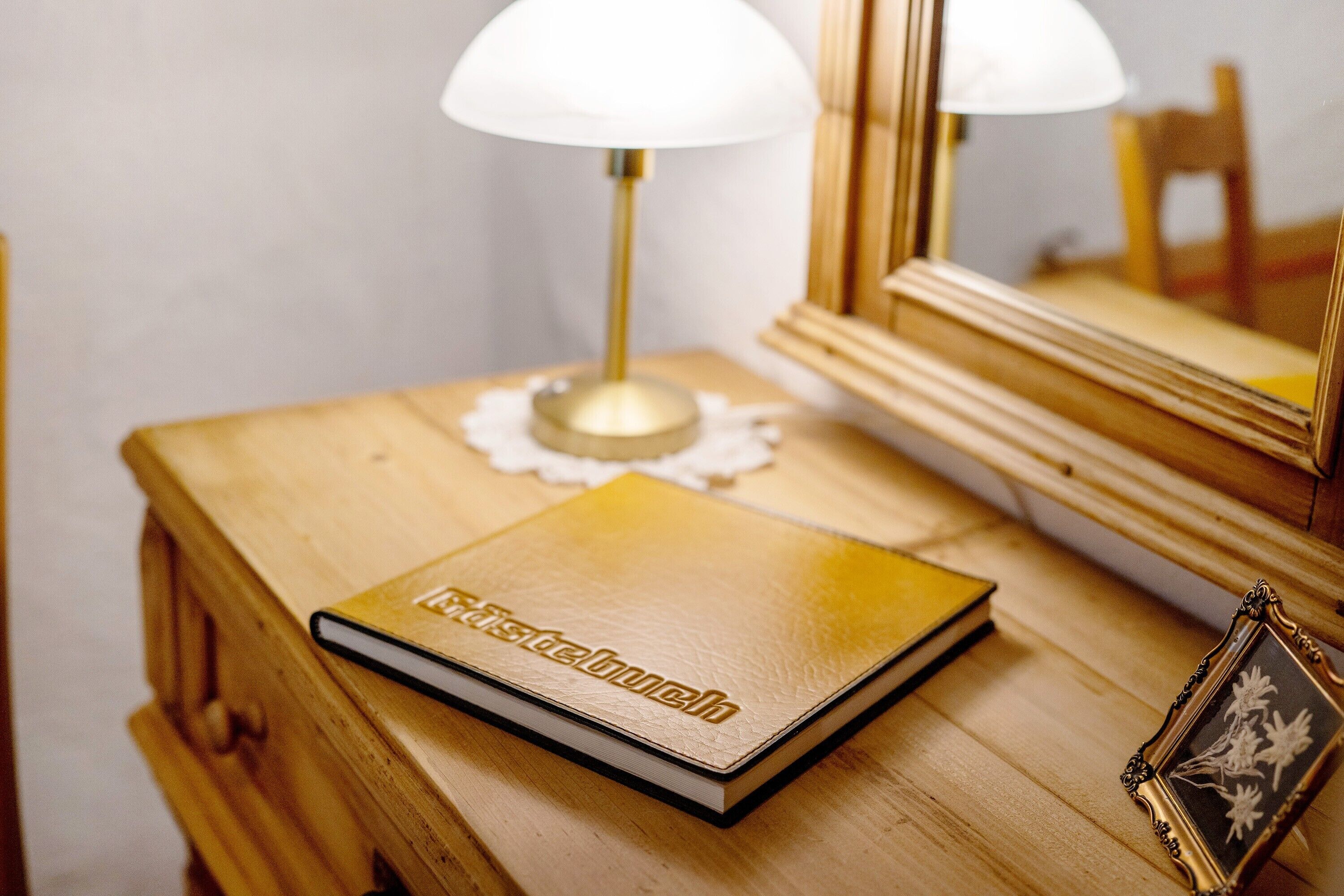 A wooden bedside table with a book, a lamp, and a framed picture.