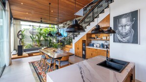 A modern kitchen with a marble countertop, wooden cabinets, and a built-in oven. - Deluxe 2-Bedroom Tropical Haven in Seminyak with Pool & Designer Interiors (Badung)