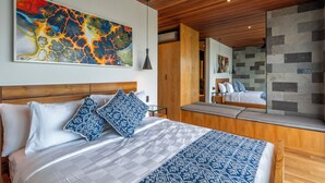 A modern bedroom with a wooden headboard, a large abstract painting, and a view of a bathroom through a glass partition. - Deluxe 2-Bedroom Tropical Haven in Seminyak with Pool & Designer Interiors (Badung)