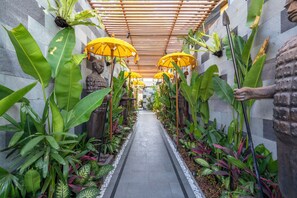 A corridor lined with large green plants and yellow umbrellas, leading to a central area with a statue. - Deluxe 2-Bedroom Tropical Haven in Seminyak with Pool & Designer Interiors (Badung)