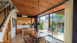 A modern kitchen with wooden cabinets, a dining area with a large table and chairs, and a view of an outdoor swimming pool. - Deluxe 2-Bedroom Tropical Haven in Seminyak with Pool & Designer Interiors (Badung)