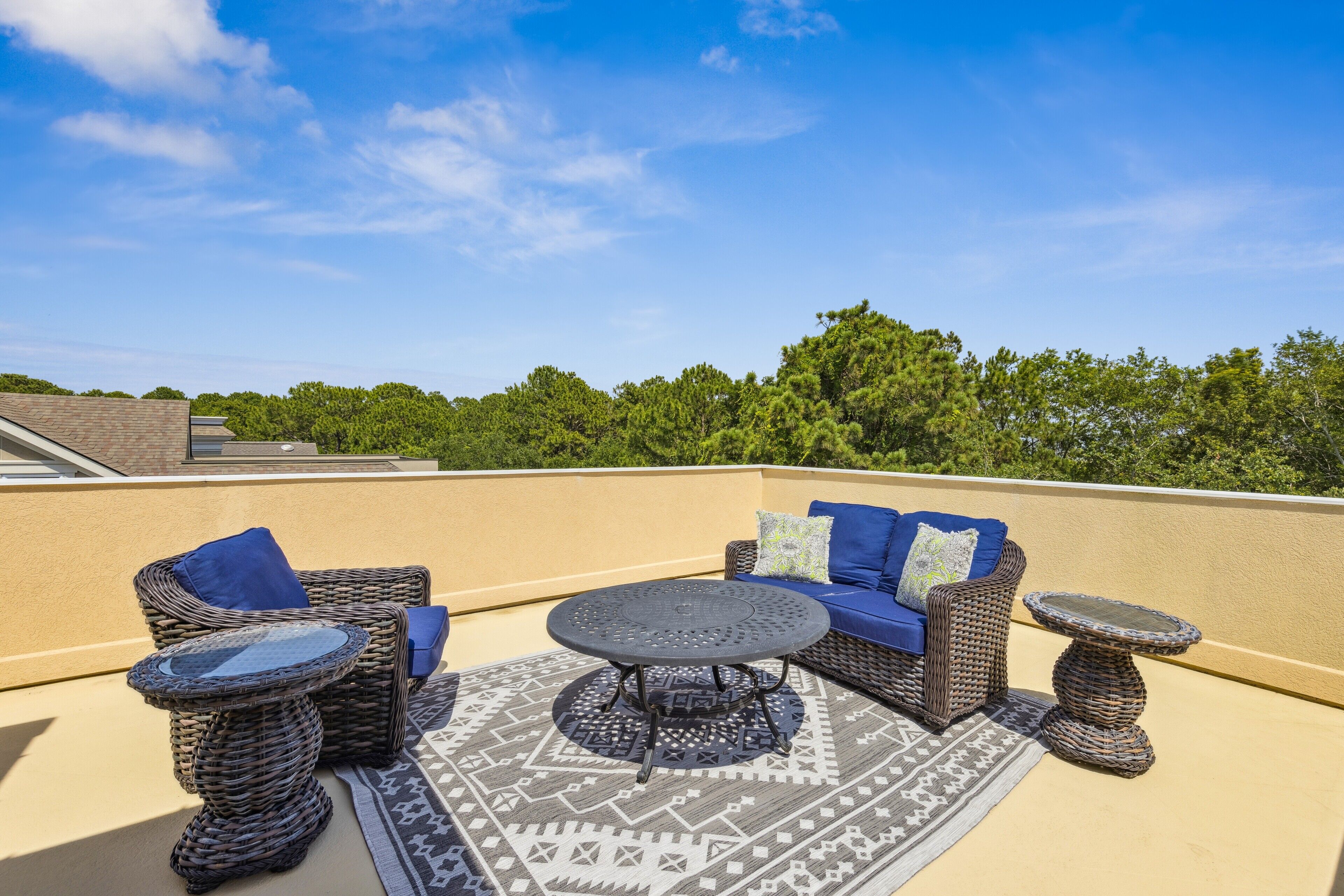 A rooftop patio with wicker furniture, a patterned rug, and a clear view of the surrounding trees.