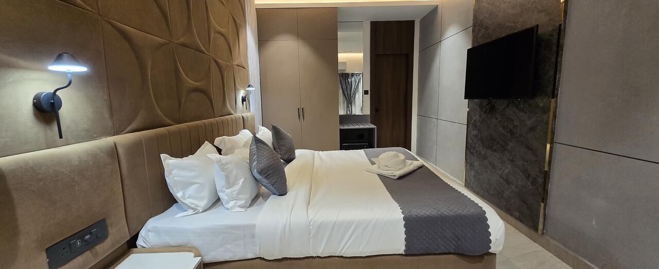 A modern hotel room with a large bed, a flat-screen TV mounted on the wall, and a built-in wardrobe.