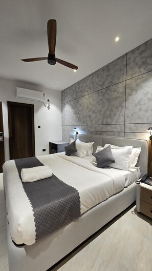 A modern bedroom with a large bed, a ceiling fan, an air conditioning unit, and a nightstand with a lamp. - Twenty Three Urban Suites (Hyderabad)