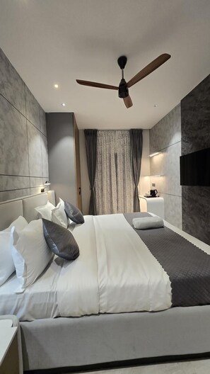 Une chambre d’hôtel moderne, dotée d’un grand lit, d’un ventilateur de plafond, d’une télévision et d’une table de chevet.