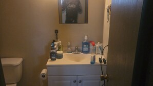 A bathroom with a toilet, sink, mirror, and various toiletries. - Charming 1-bedroom apartment in serene Elyria with AC (Elyria)