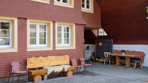 A building with a red brick exterior, a wooden bench, two chairs, a table, and a small potted plant. - Apartment 'Alte Schmiede 2 Apartments' with Mountain View, Private Terrace and Wi-Fi (Feldberg (Schwarzwald))