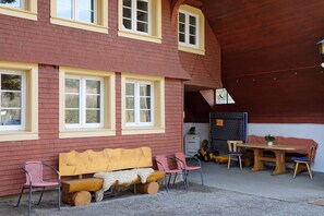 A building with a red brick exterior, a wooden bench, two chairs, a table, and a small potted plant. - Apartment 'Alte Schmiede 2 Apartments' with Mountain View, Private Terrace and Wi-Fi (Feldberg (Schwarzwald))