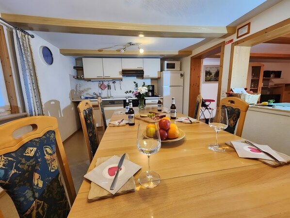 A dining area with a wooden table, chairs, a fruit bowl, wine glasses, and a ceiling fan.