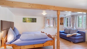 A wooden bed with a headboard, a blue sofa, and a window with curtains. - Apartment 'Alte Schmiede 2 Apartments' with Mountain View, Private Terrace and Wi-Fi (Feldberg (Schwarzwald))