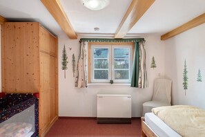 Een kamer met een bed, een radiator, een raam met gordijnen, een stoel en een kledingkast.