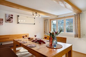 Un comedor con una mesa de madera, sillas, un banco y una ventana con cortinas.