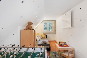 A children's room with a bed, a small table with toys, a foosball table, and a window with curtains.