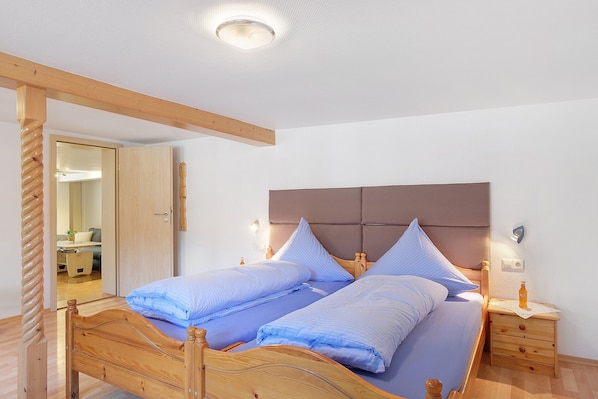 Una cama doble con cabecera de madera, dos mesitas de noche con lámparas, y suelo de madera.