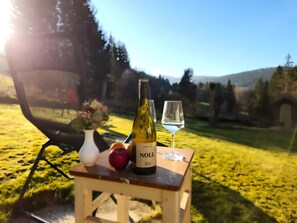 A table with a bottle of wine, a glass, an apple, and a vase with flowers.