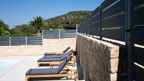 A poolside area with lounge chairs and a stone wall. - Newly built detached house, private pool, sea views, Aegina, 400m from the beach (Aegina Agioi)