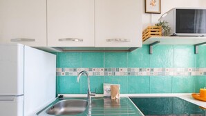 A kitchen with white cabinets, a sink, a microwave, and a teal backsplash. - Porto Marina by Rentbeat (Villanova di Ostuni)