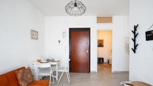 A modern living room with a sofa, dining table, chairs, a wooden door, and a hallway leading to a bedroom. - Porto Marina by Rentbeat (Villanova di Ostuni)