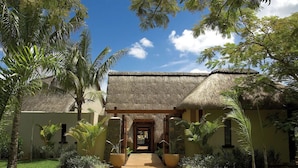 Un resort con un edificio de techo de paja, un camino pavimentado y exuberante vegetación tropical.