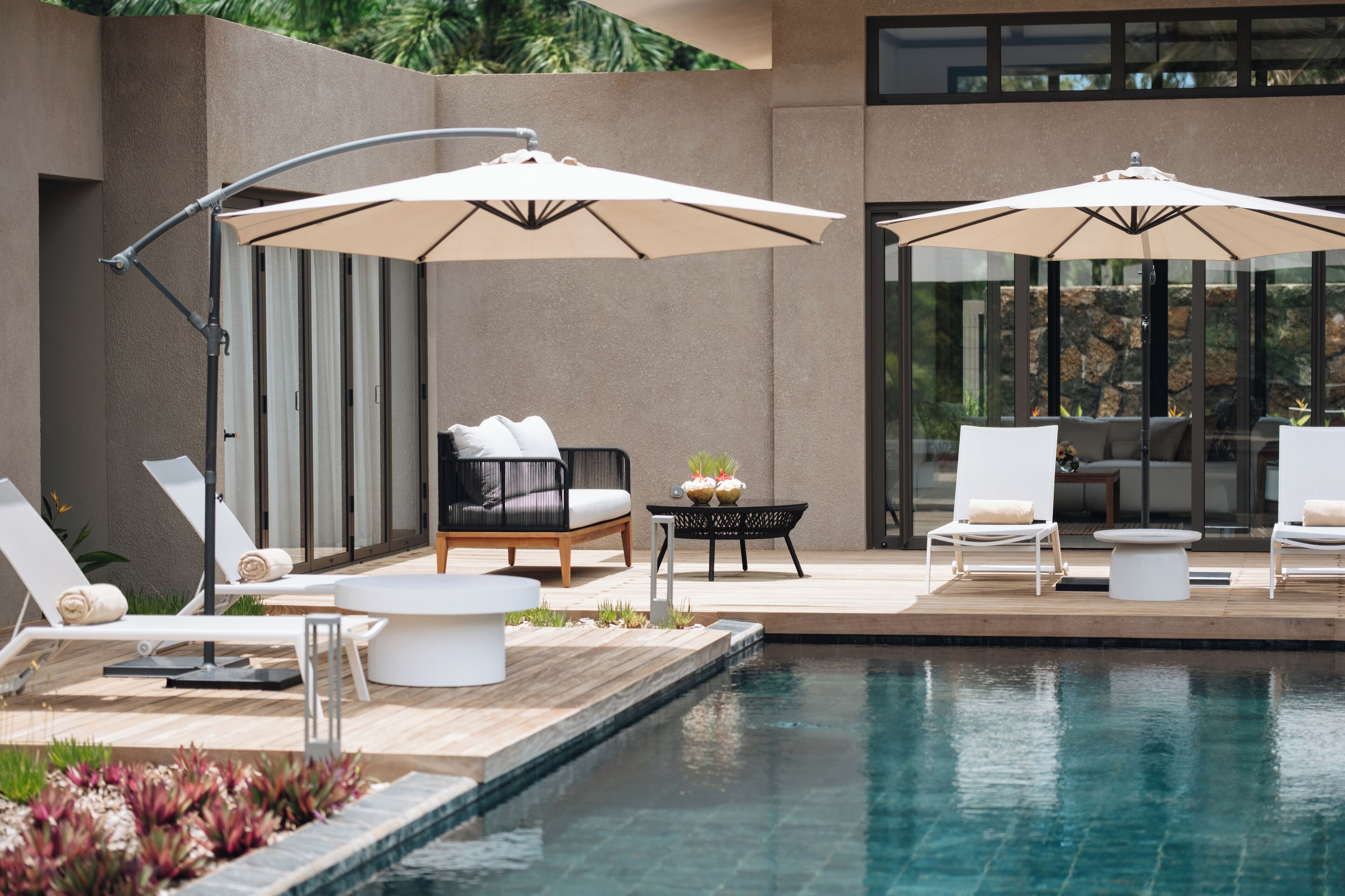 Zona junto a la piscina con sillones de descanso, sombrillas y una mesa con una planta.