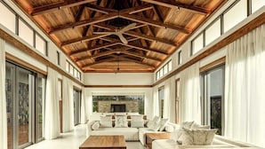Un salón espacioso con techo alto y vigas de madera, ventanas amplias y chimenea.