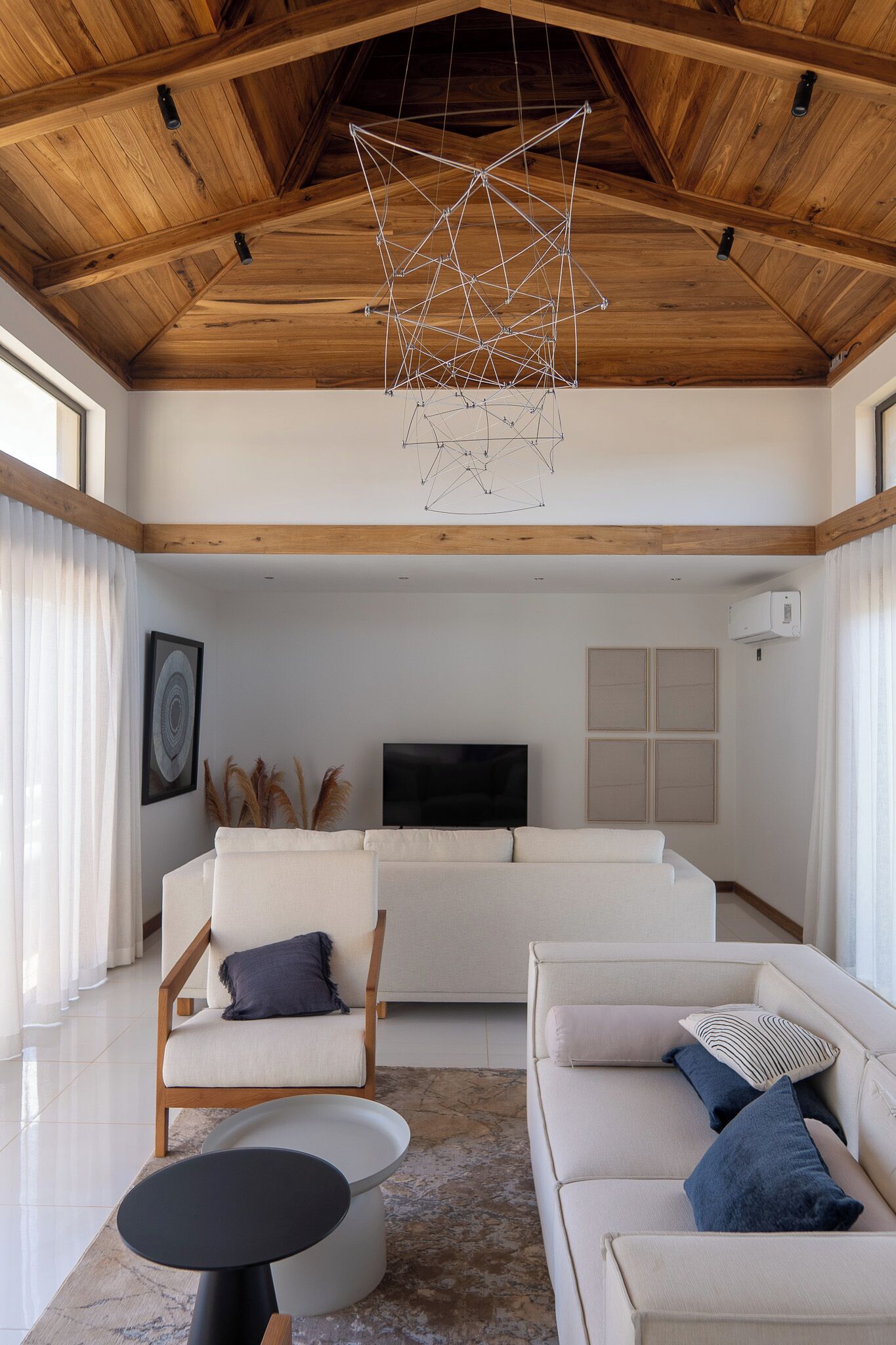 Een moderne woonkamer met een houten plafond, een witte bank, een ronde zwarte tafel en een televisie aan de muur.