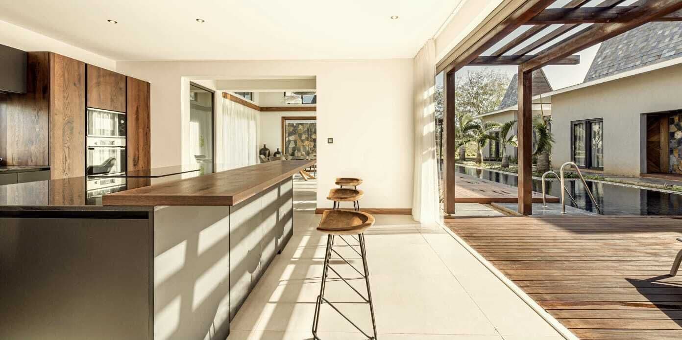 Una cocina moderna con una isla central, taburetes de bar y vistas a la terraza exterior.