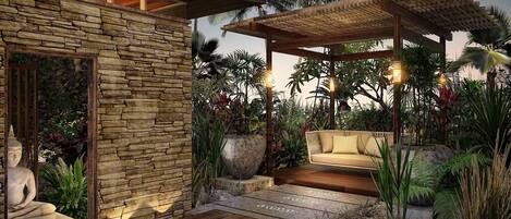 A modern outdoor patio with a stone wall, a wooden deck, and a cushioned seating area surrounded by tropical plants.