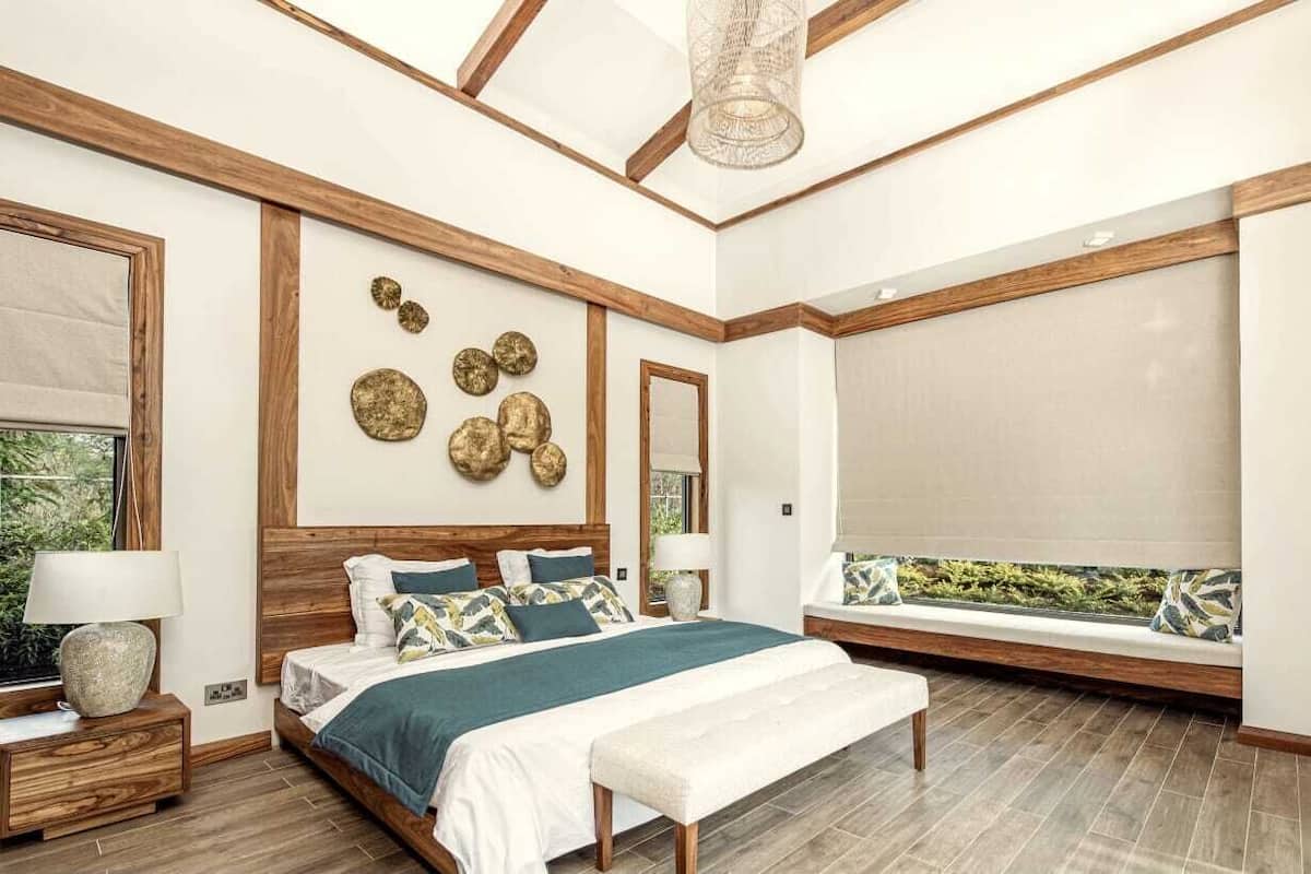 Une chambre avec un grand lit, un banc près de la fenêtre et un ventilateur de plafond.