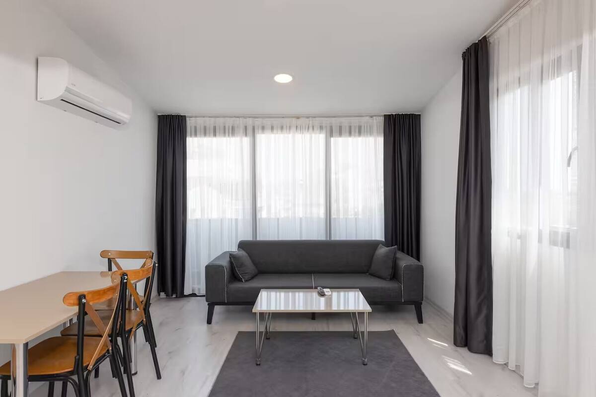 A modern living room with a sofa, a coffee table, a dining table with chairs, and an air conditioning unit.