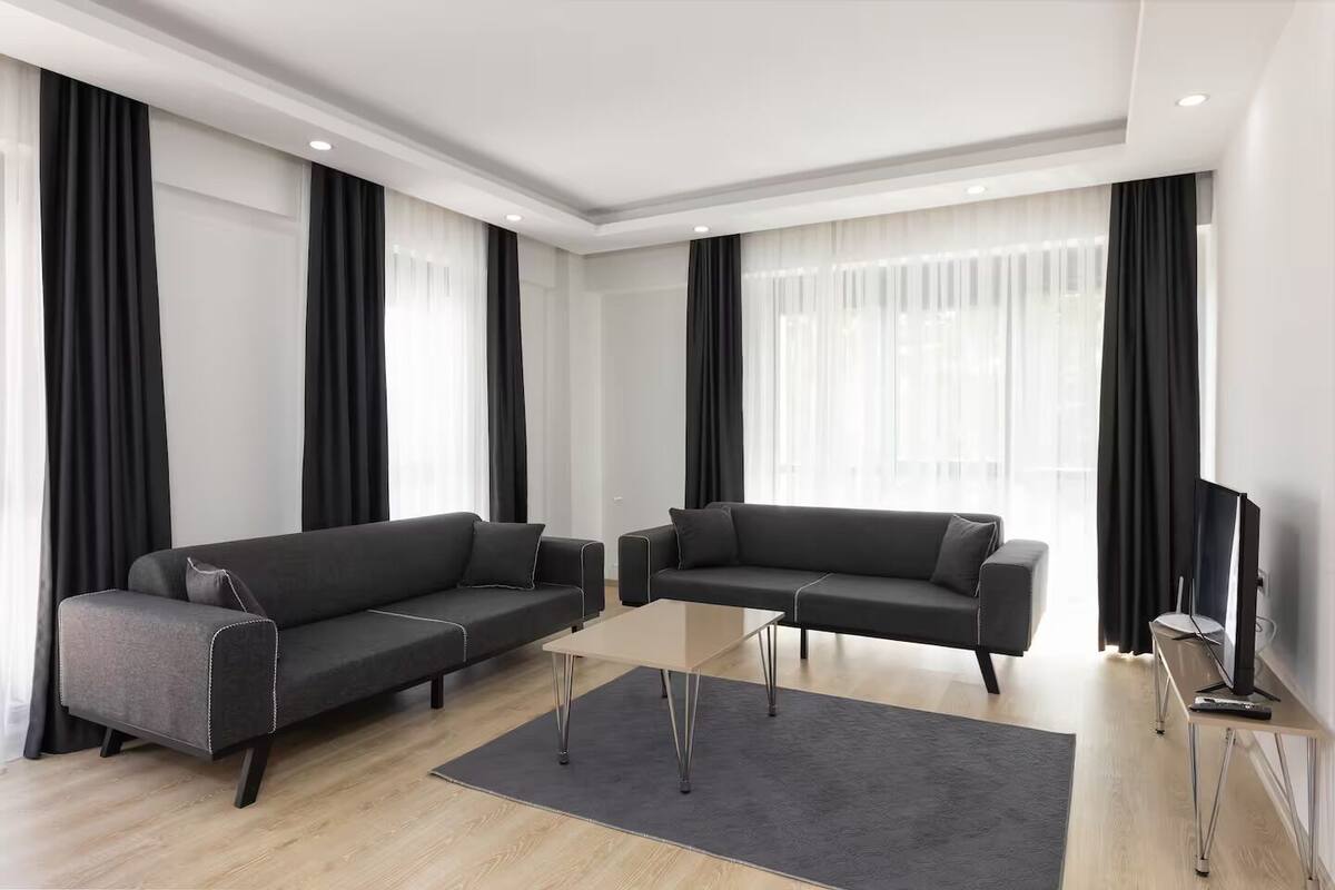 A modern living room with two dark sofas, a glass coffee table, and a flat-screen TV on a stand.