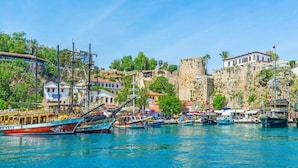 A coastal town with historic stone buildings, a fortified structure, and boats docked along the waterfront. - Moon Old Town (Antalya)