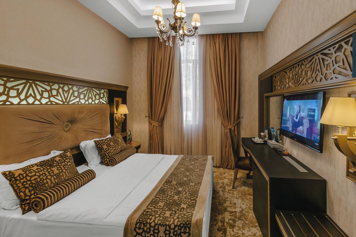 A hotel room with a large bed, a television, a desk, and a chandelier.