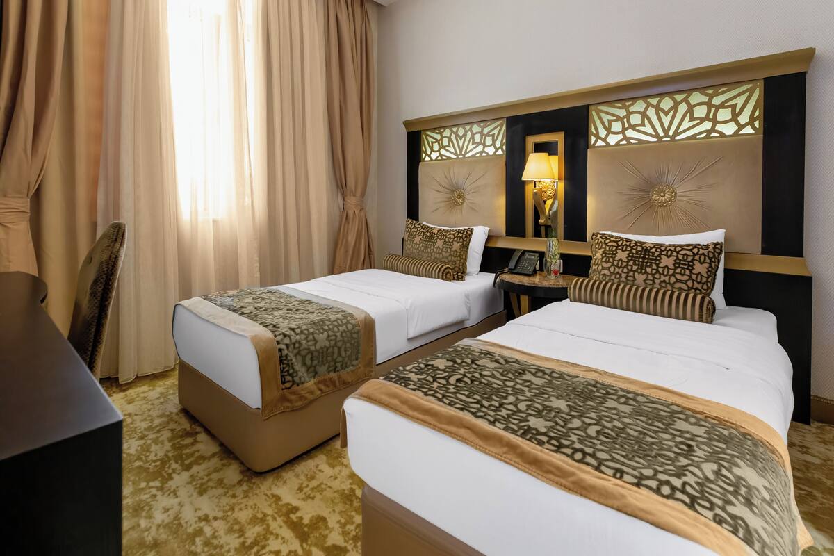 A hotel room with two beds, a desk, a chair, and a large window with curtains.
