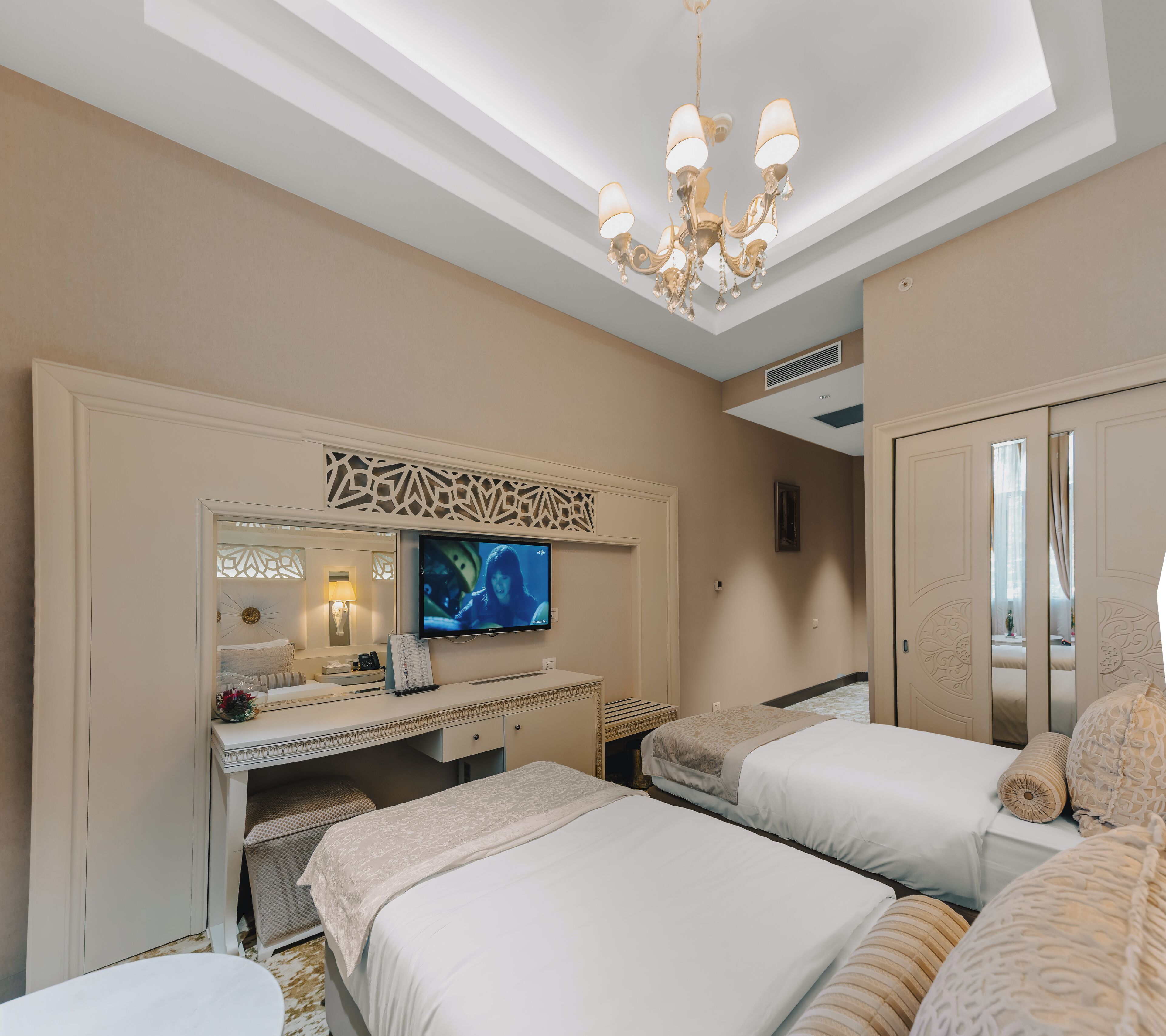 A hotel room with a large bed, a desk with a television, and a chandelier.
