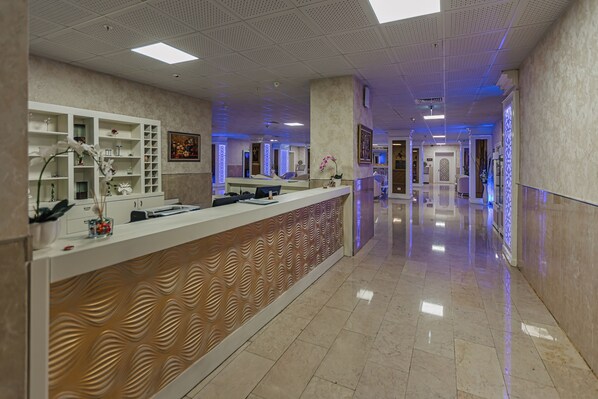 Un espace d’accueil d’hôtel au design moderne, comprenant un comptoir d’accueil, un mur décoré d’un motif original et un vaste couloir doté d’un sol poli.