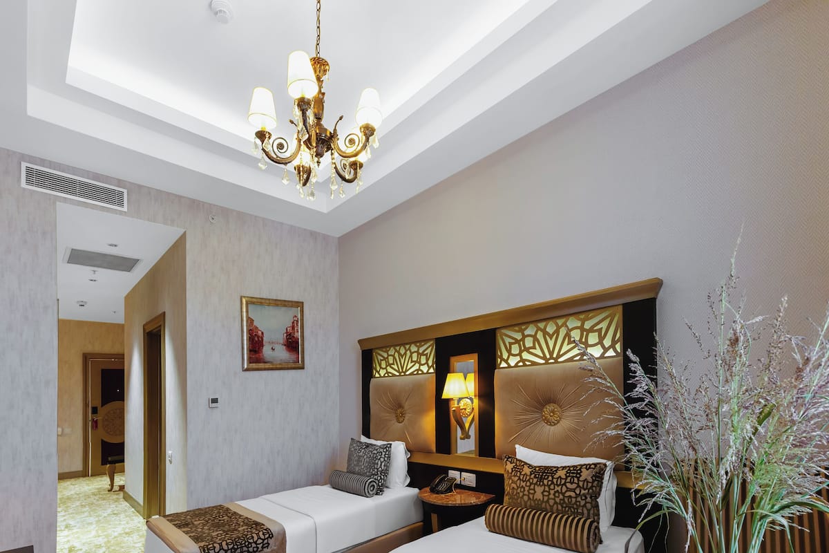 A hotel room with two beds, a chandelier, a nightstand, and a decorative plant.
