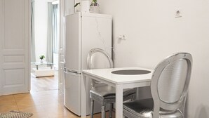 A small, modern kitchen with a white refrigerator, a dining table, and a chair. - Comfort 2BR Apt Long Stay Friendly (Vienna)