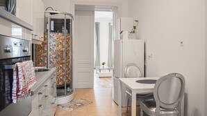 A modern kitchen with a built-in oven, a glass shower enclosure, and a dining area with a white table and chairs. - Comfort 2BR Apt Long Stay Friendly (Vienna)