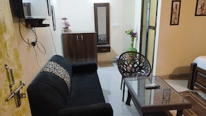 A living room with a sofa, a glass coffee table, a chair, and a small table with a vase. - The Palash Vann Resort (Kurai)