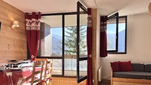Une pièce chaleureuse avec une table à manger dressée pour deux personnes, un canapé et de grandes fenêtres offrant une vue sur les montagnes.