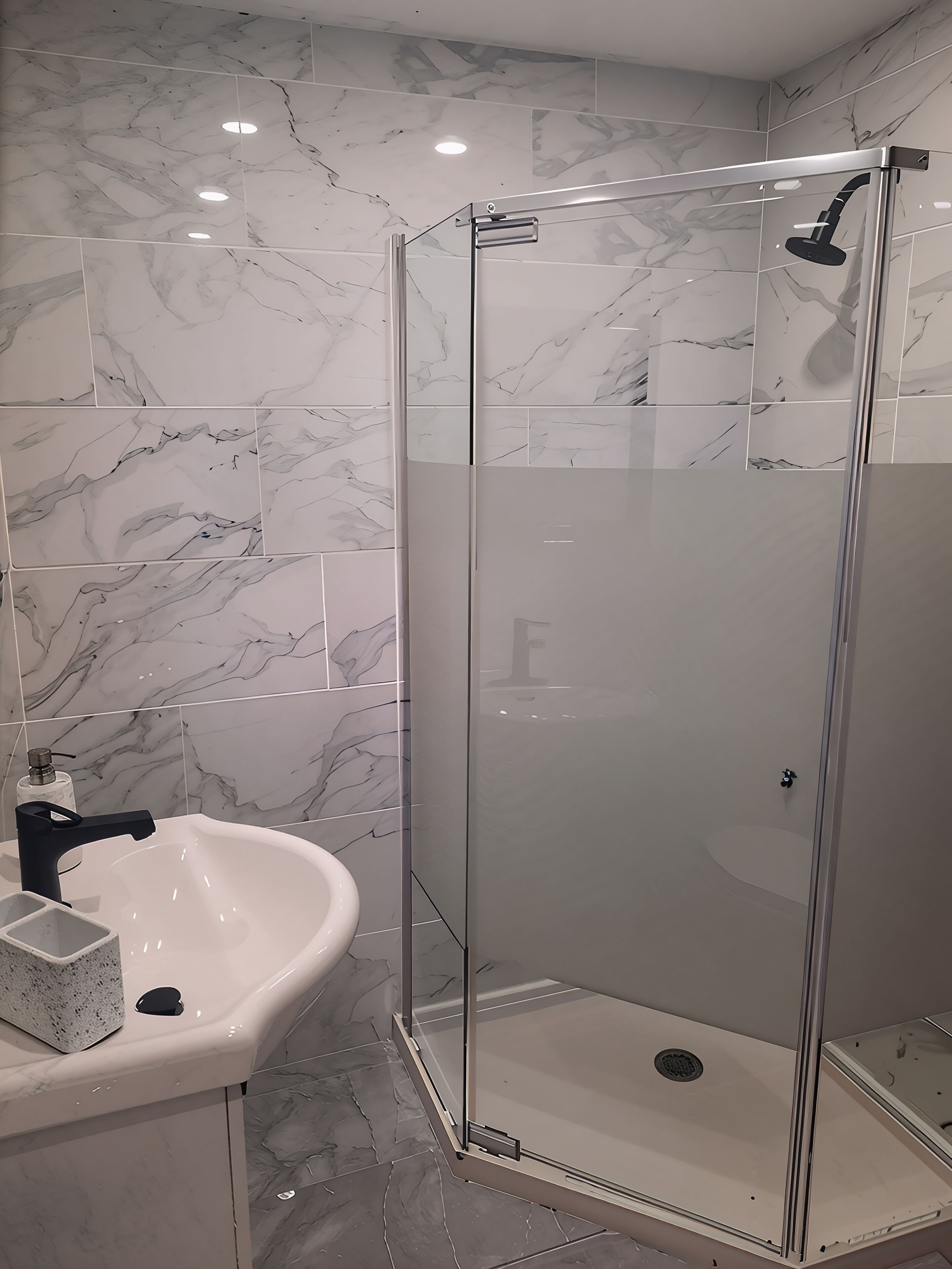 Une salle de bain dotée d’une douche à parois de verre, d’un lavabo blanc et de carreaux à motifs de marbre.