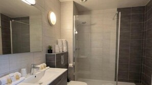 A modern bathroom with a vanity, sink, mirror, and shower area. - Logis Hotels Les Colonnes Strasbourg Zénith (Eckbolsheim)