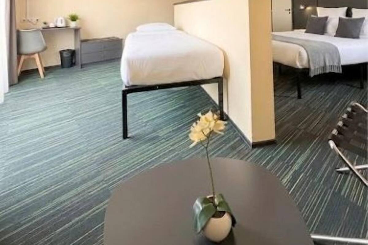 Hotellihuone, jossa on sänky, työpöytä, tuoli, pieni pöytä maljakolla ja seinälle asennettu televisio.