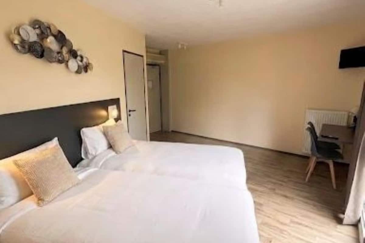 Hotellihuone, jossa on suuri sänky, seinälle asennettu televisio ja ovi, joka johtaa toiseen huoneeseen.