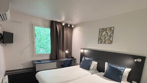 A double bed with a headboard, a desk with a chair, a window with curtains, and a wall-mounted TV. - Logis Hotels Les Colonnes Strasbourg Zénith (Eckbolsheim)