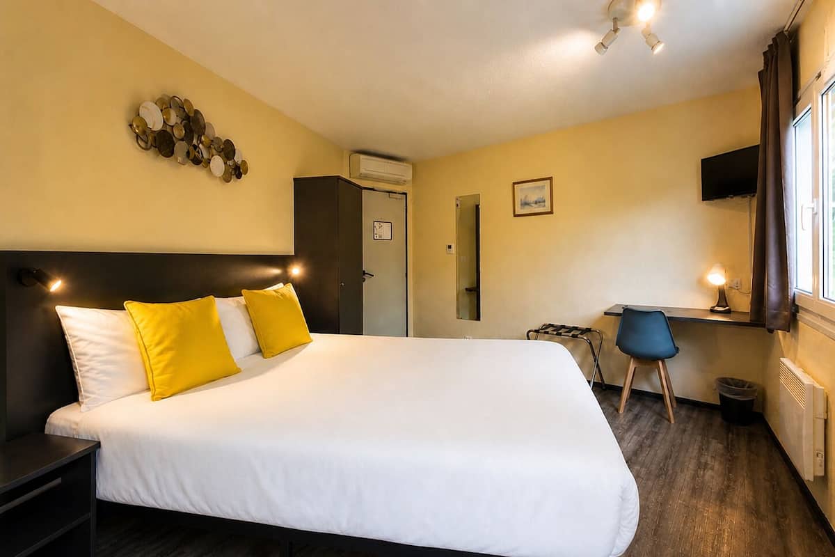 Hotellihuone, jossa on sänky, työpöytä, tuoli, televisio ja ilmastointilaite.