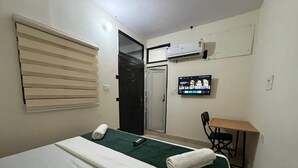A hotel room with a bed, a desk, a chair, an air conditioner, and a TV on the wall. - The Harikanta Residency (New Delhi)