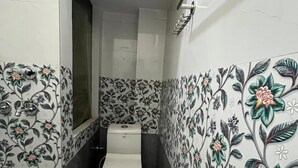 A small bathroom with a toilet, a shower, and tiled walls with floral patterns. - The Harikanta Residency (New Delhi)